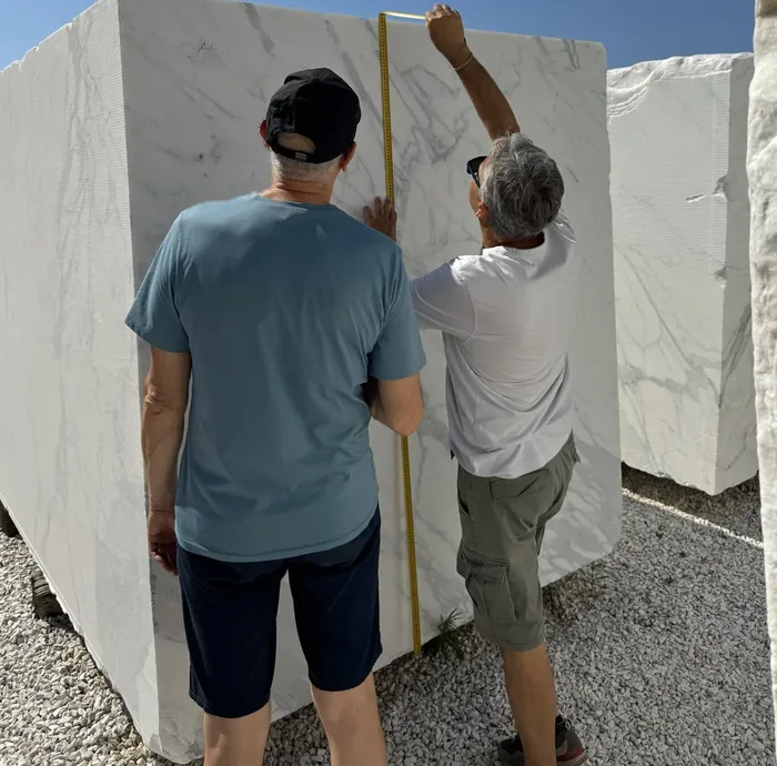 Two people measuring a white marble block with a folding rule in the block yard
