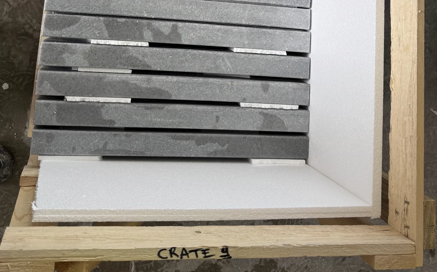 Open numbered crate seen from above with stone pieces packed on edge between foam liners