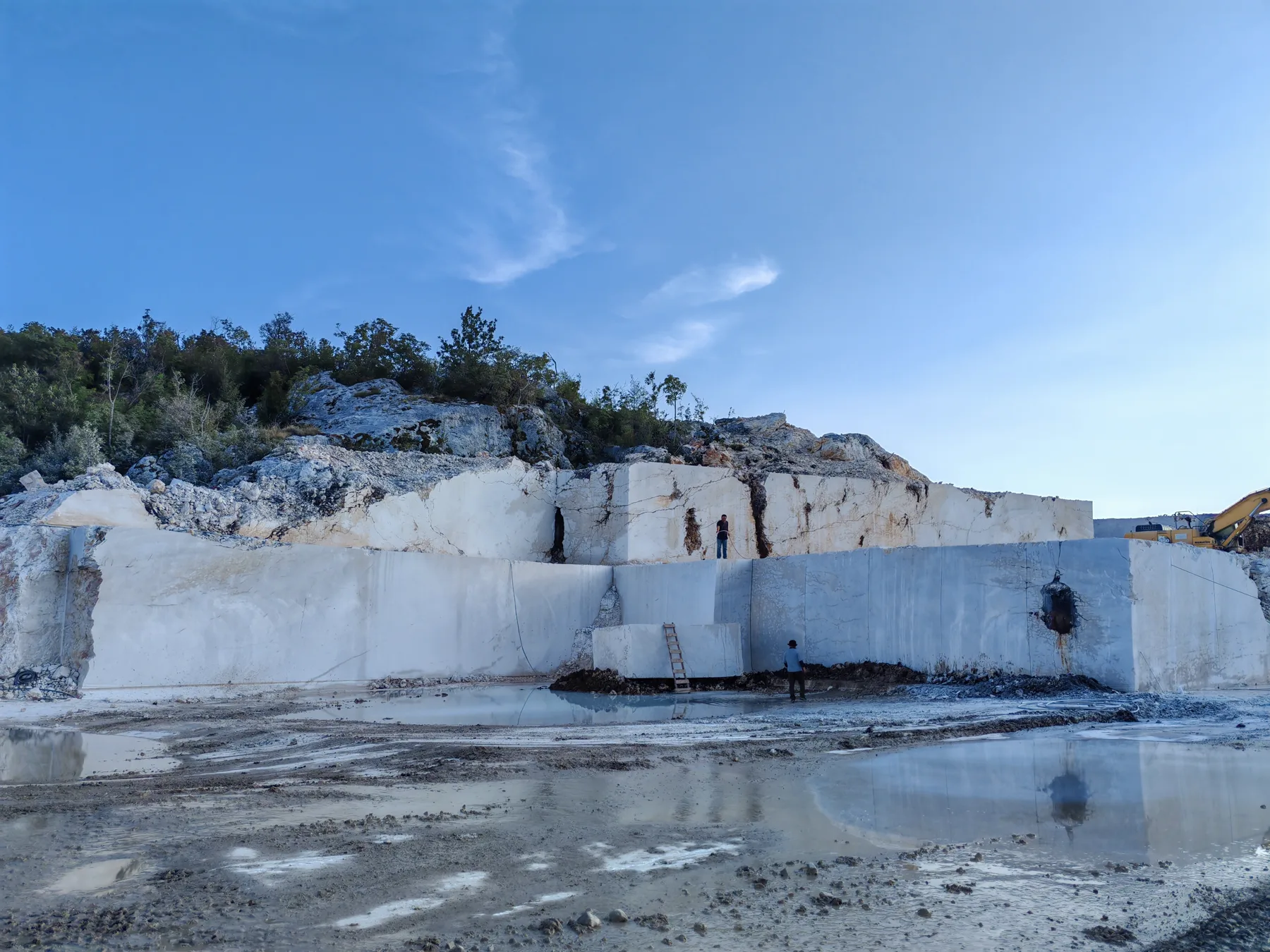 Quarry front with sawn stone benches, two workers reading the face before block selection