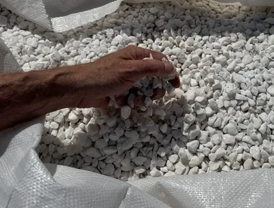 Hand checking white marble aggregate inside a bulk bag