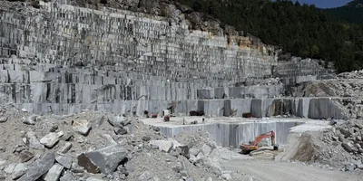Quarry face worked in benches, gray stone, excavator at the foot of the wall