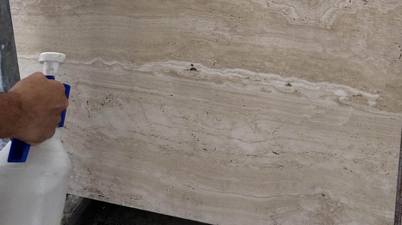 Wetting a travertine slab with a hand sprayer to read tone and vein during selection