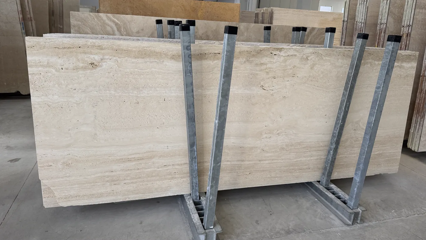 A full travertine slab standing on steel stands in a warehouse aisle