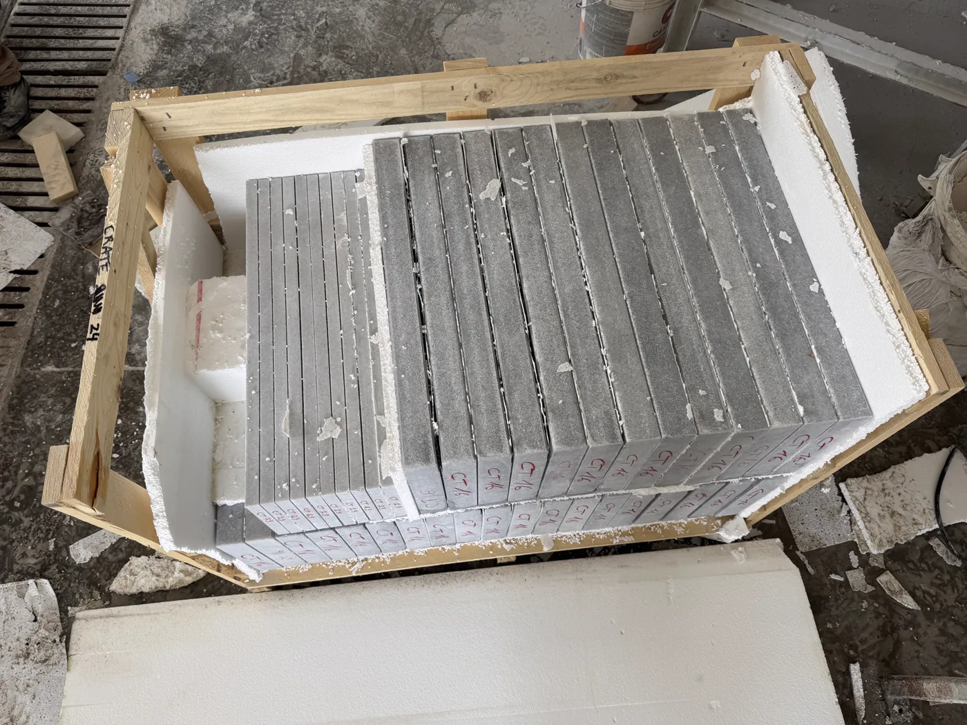 Open crate with grey stone copings packed on edge between foam separators, each piece marked