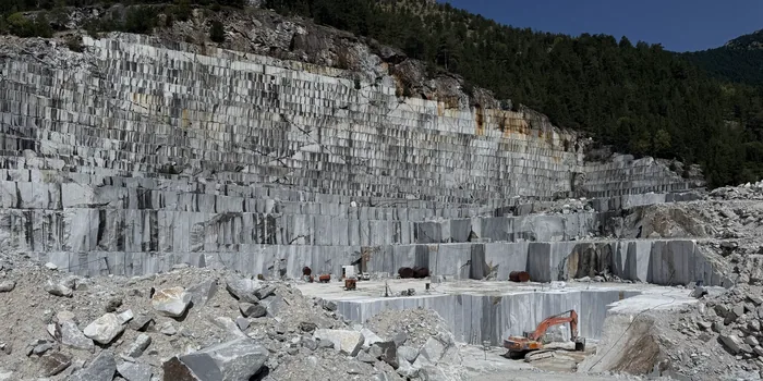 Open quarry face with sawn benches and a cut block on the floor
