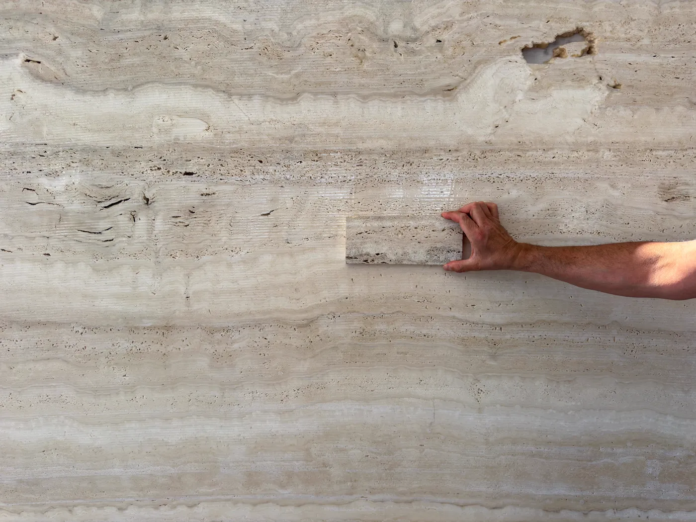 Hand holding a stone sample against the face of a full slab to confirm the material