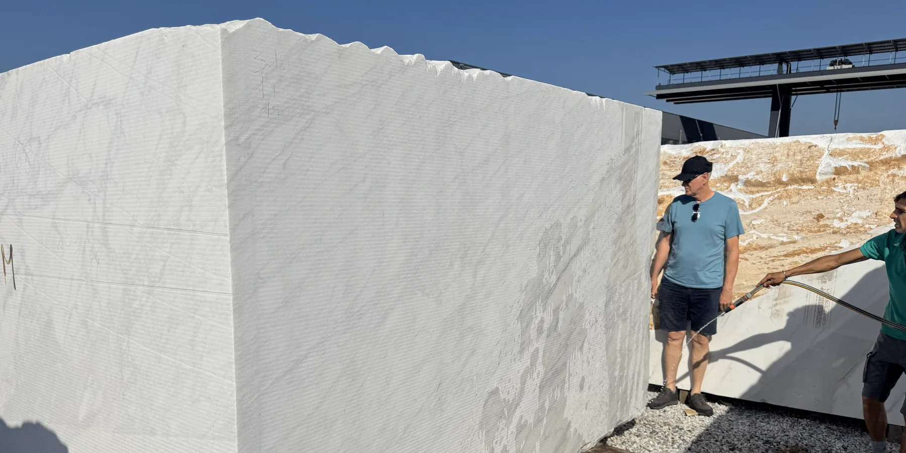 Oversized white marble block in the yard, two people alongside for scale
