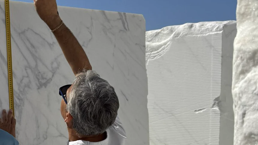 Measuring the height of an oversized white marble block with a tape during on-site selection