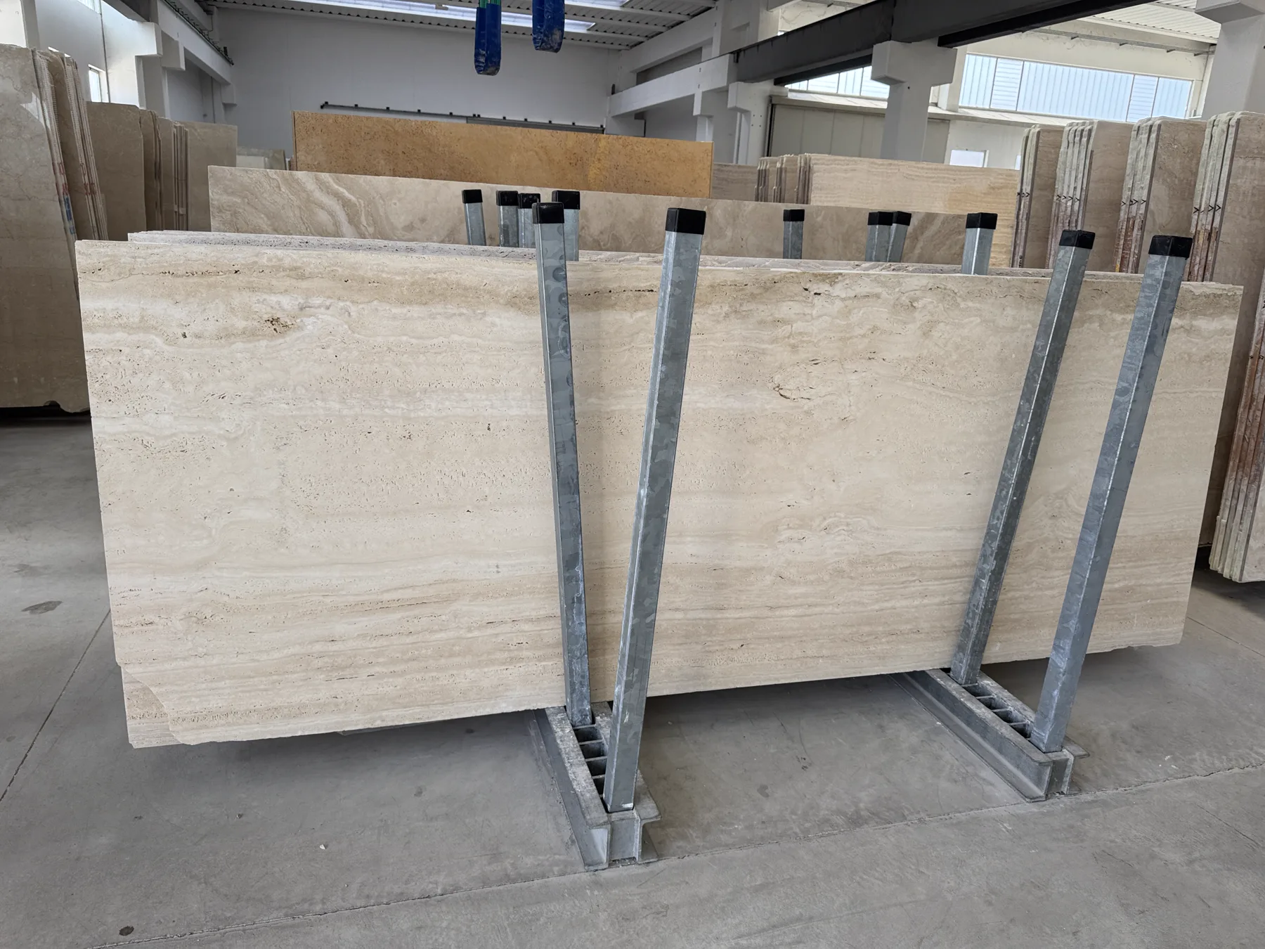 Vein-cut travertine slabs racked whole on A-frames for screening before cutting