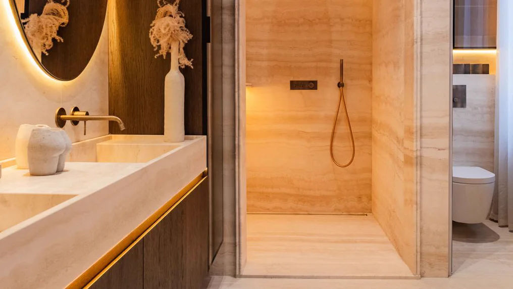 Finished travertine bathroom with large-format wall panels, carved basins and a matching floor