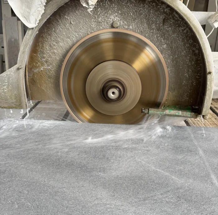Diamond blade cutting a grey stone slab under running water on the bridge saw