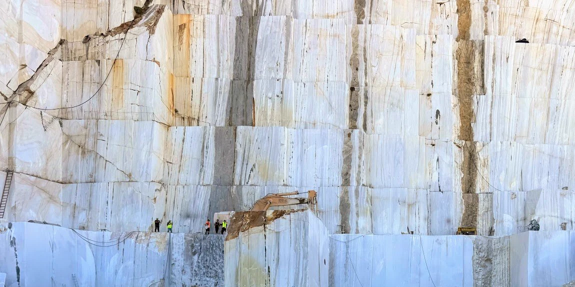 Benched face of a white marble quarry, crews at the foot of the wall for scale