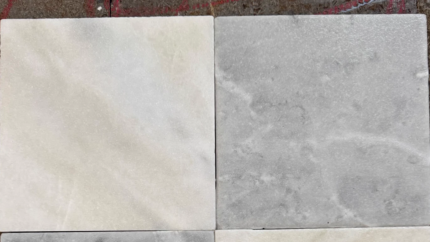 Tumbled white and gray stone sample tiles compared side by side during finish review