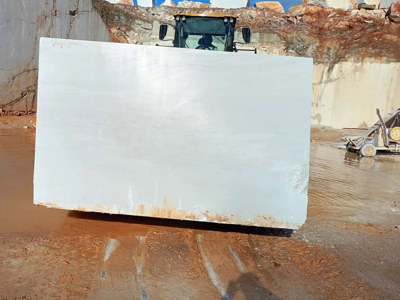 Squared white marble block on the quarry floor, wheel loader behind it for scale