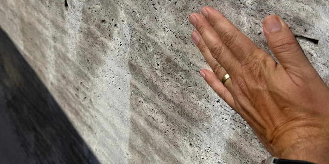 Bare hand reading the raw sawn face of a stone block during selection